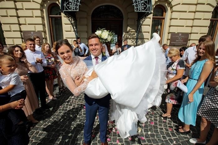 Жених поднимает невесту на руки, выходя из ЗАГСа.